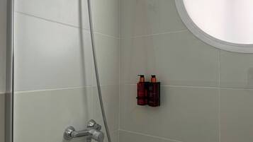 Une douche équipée d’un pommeau de douche à main et d’un robinet mural. Deux flacons de shampoing et d’après-shampoing sont posés sur une petite étagère.