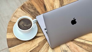 Una computadora portátil y una taza de café sobre una mesa redonda de madera.