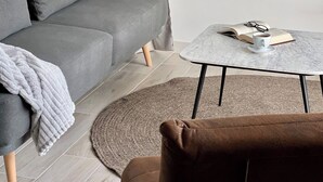 Una sala de estar moderna con un sofá gris, un tapete redondo, una mesita de centro pequeña y una silla marrón.