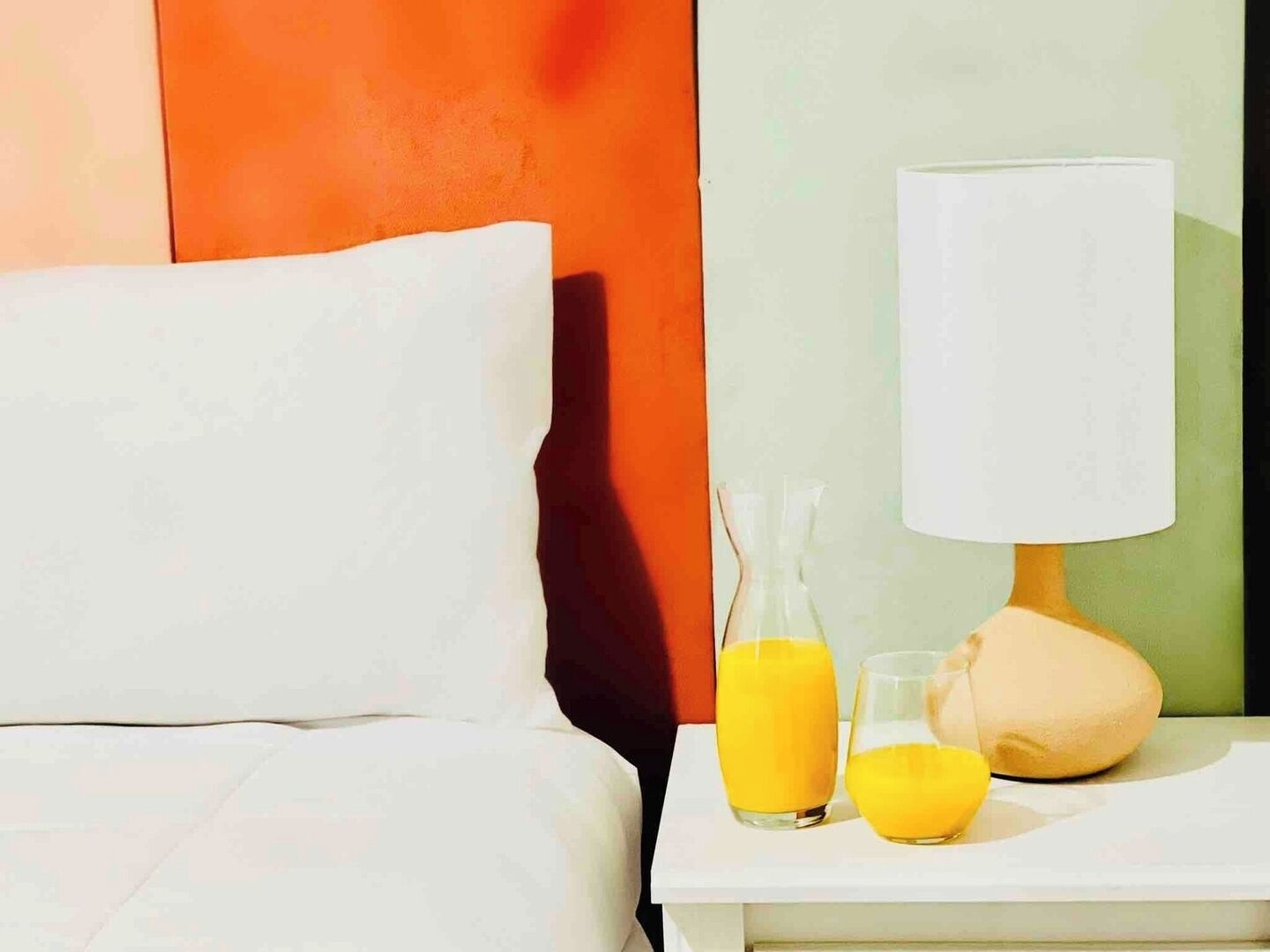 A hotel room with a bed, a nightstand, a lamp, and two glasses of orange juice.