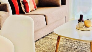 A modern living room with a beige sofa, white armchair, and a round coffee table with decorative items. - Canaryislandshost l Mar Lanzarote (Puerto del Carmen)