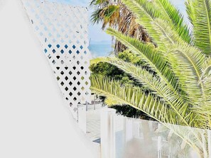 A white lattice fence with diamond-shaped openings, palm trees, and a clear sky.