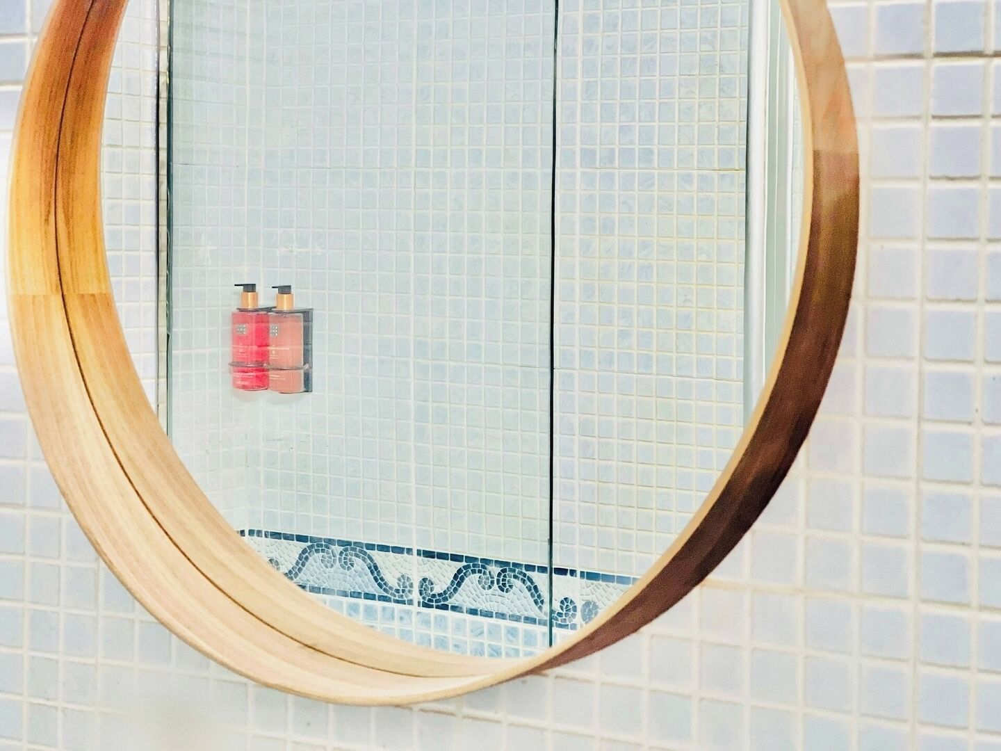 Ein Badezimmer mit Fliesenwand, einem spiegel mit Holzrahmen und zwei Seifenflaschen.