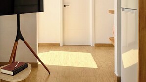 Une chambre moderne équipée d’un téléviseur à écran plat posé sur un meuble, d’une porte fermée et d’un réfrigérateur blanc.