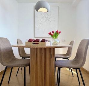 A modern dining area with a wooden table, four grey upholstered chairs, a vase with red tulips, and a pendant light. - Canaryislandshost l Orilla III (Caleta de Famara)