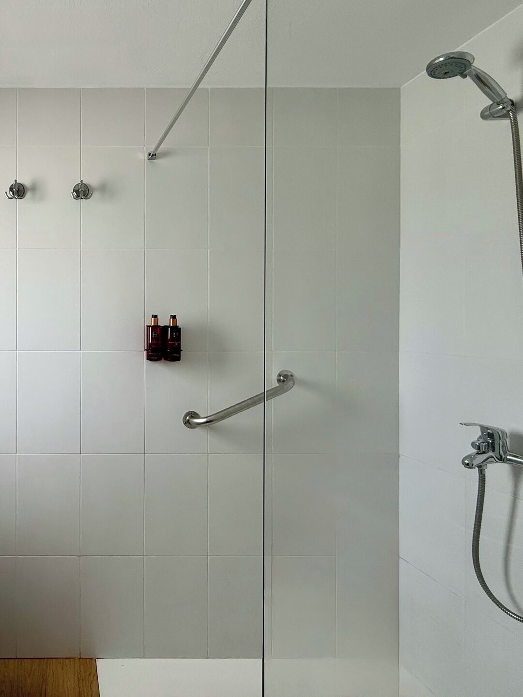 A modern shower area with a glass door, a handheld showerhead, and a handheld faucet.