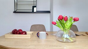 Une table de salle à manger en bois, ornée d’un vase de tulipes rouges, d’un saladier en bois rempli de fruits et d’une tasse à rayures.