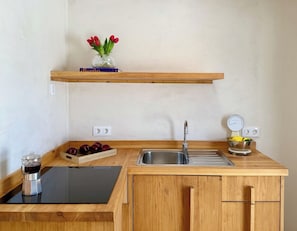 A kitchen with a wooden countertop, a sink, a coffee maker, a bowl of lemons, and a vase with red flowers. - Canaryislandshost l Orilla III (Caleta de Famara)