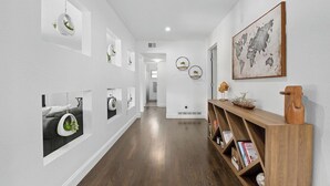 Un pasillo con paredes blancas, piso de madera y una estantería de madera con libros y objetos decorativos.