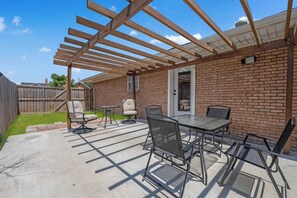 En uteplats med en pergola, utomhusmöbler och en mur av tegelsten.