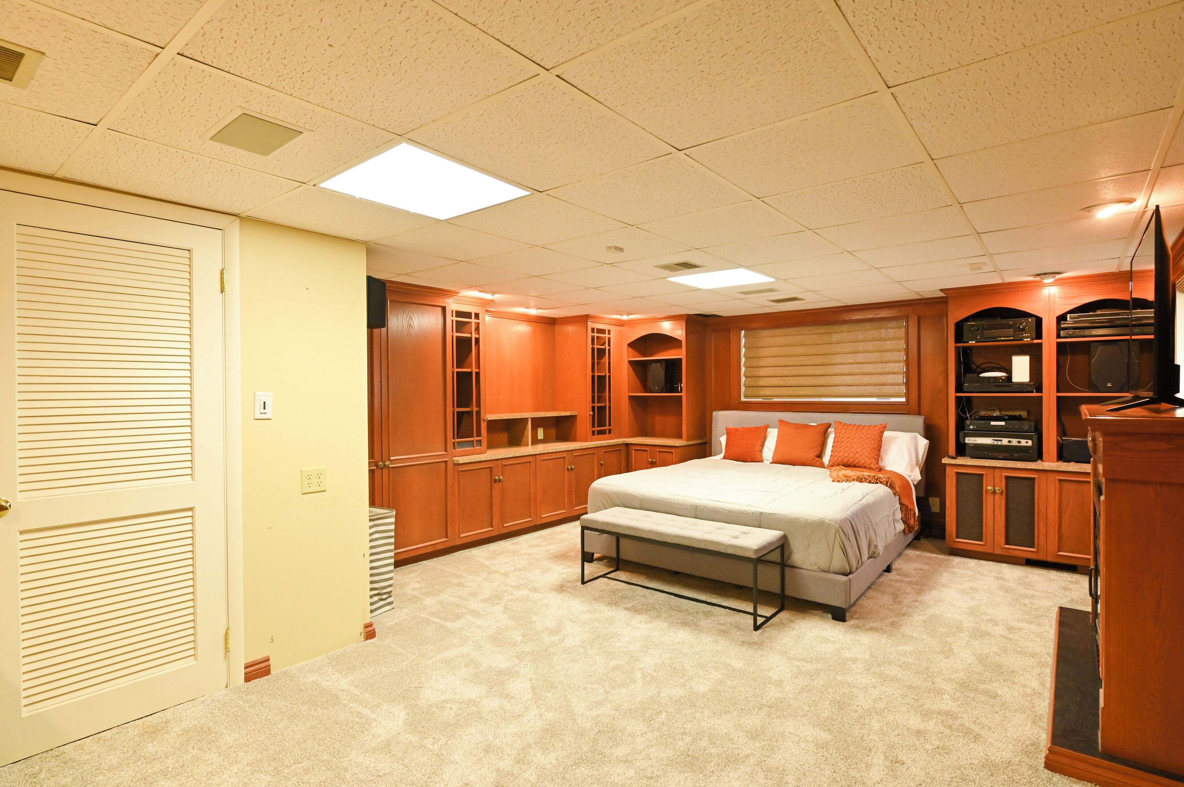 A bedroom with a bed, bench, built-in shelving, and a television.