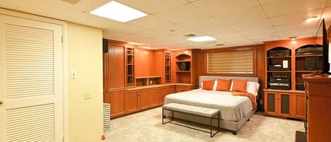 A bedroom with a bed, bench, built-in shelving, and a television.