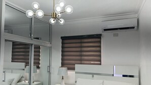 Een slaapkamer met een bed, nachtkastjes, een spiegel, een plafondlamp en een raam met jaloezieën.
