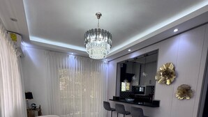 Een moderne woonkamer met een gebogen bank, een eethoek met barstoelen, een kroonluchter en een marmeren vloer.