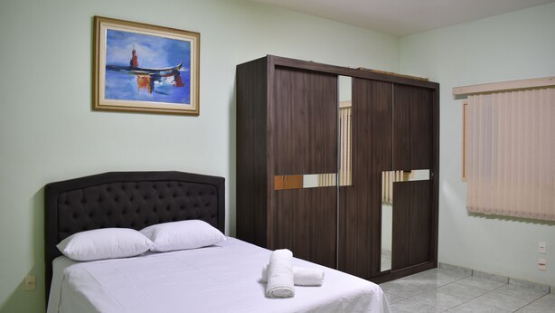 A neatly made bed with white linens and pillows, a dark wooden wardrobe, and a framed painting on the wall. - Canastra Ebenezer House in Vargem Bonita, MG (Vargem Bonita)