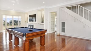 Amplia sala de estar con mesa de billar, chimenea y escalera que sube a un nivel superior.
