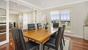 Un comedor con mesa de madera y sillas negras, ventanas amplias con vistas, y una orquídea en maceta sobre la mesa.