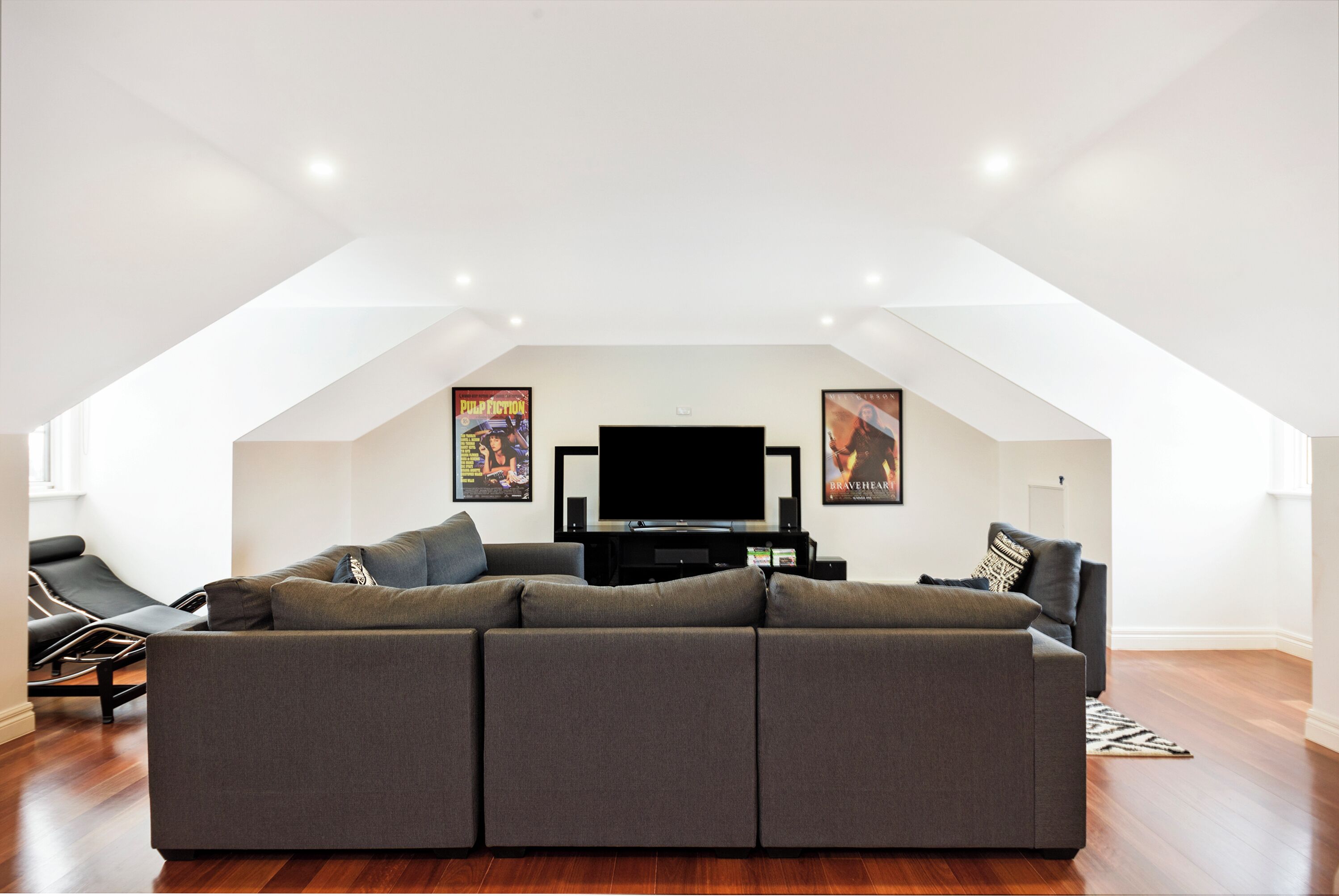 A modern living room with a sectional sofa, a flat-screen TV, and two posters on the wall.