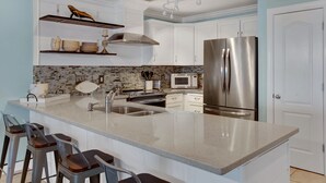 Een moderne keuken met witte kasten, een roestvrijstalen koelkast, een magnetron en een groot eiland met barstoelen.