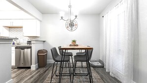Una cocina compacta con lavavajillas, una pequeña mesa de comedor con sillas, un reloj y una planta en maceta.