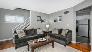 Una sala de estar moderna con un juego de sofá gris, una mesa de centro y una escalera que conduce a otro nivel.