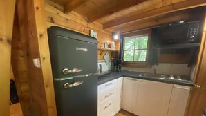 A compact kitchen with wooden walls, a black refrigerator, white cabinets, and a window with a view of greenery. - 1 Bedroom Chalet in Le Buisson de Cadouin (Le Buisson de Cadouin)