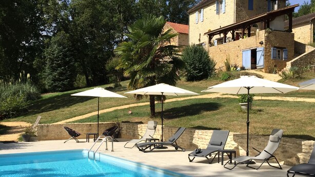A pool area with lounge chairs and umbrellas, surrounded by a stone wall and greenery. - 1 Bedroom Chalet in Le Buisson de Cadouin (Le Buisson de Cadouin)