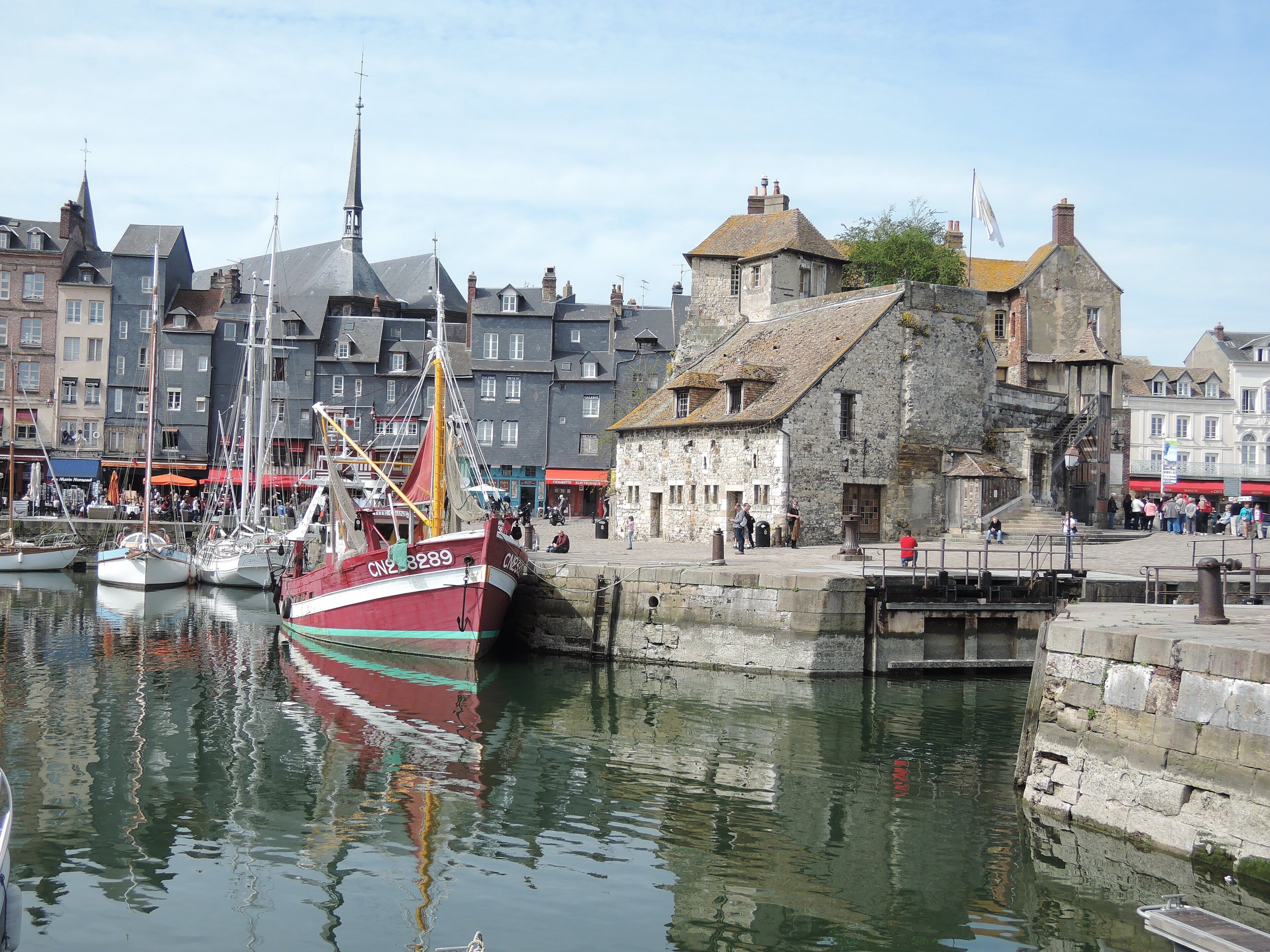 Un port où sont amarrés des bateaux, des bâtiments historiques en pierre et un ciel dégagé.