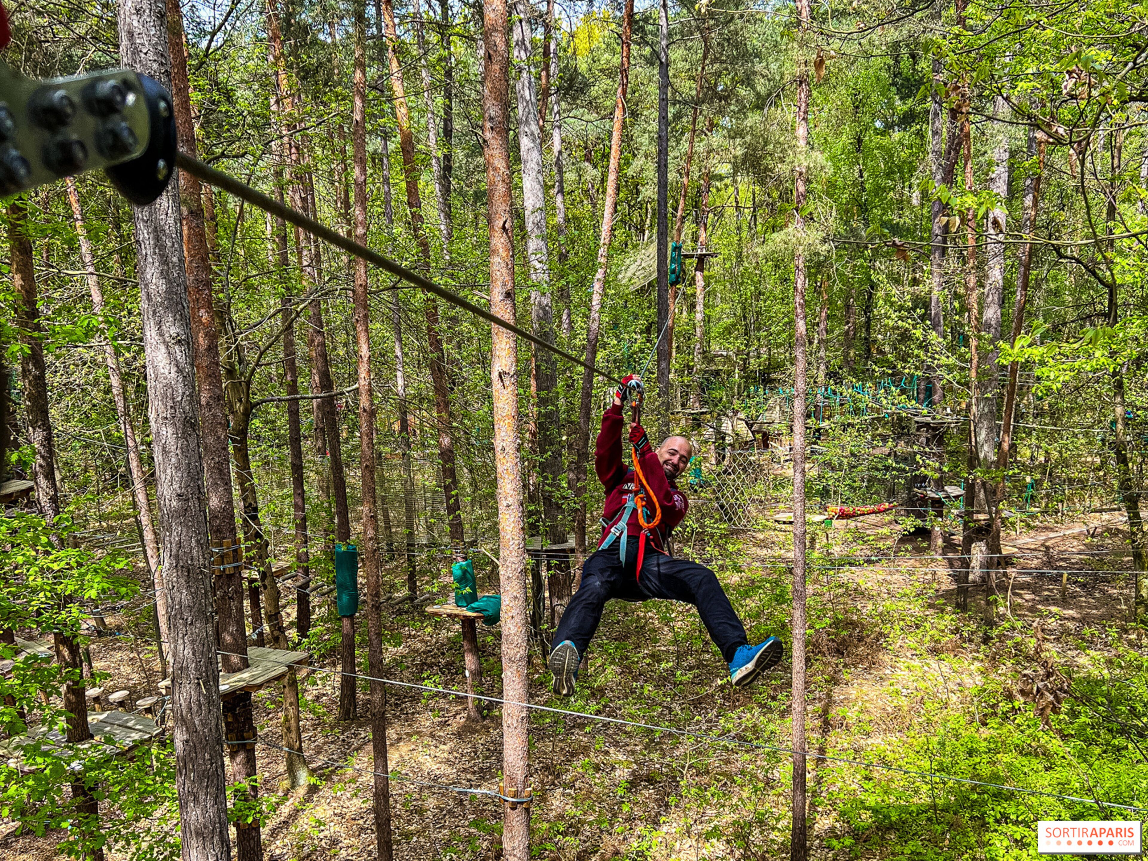 Eine Person zipline durch einen Wald mit natürlichen Holzplattformen und Sicherheitsnetzen.
