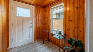 Ein Zimmer mit Holzwänden, einer weißen Tür, einem Fenster und einem kleinen Tisch mit einer Lampe.