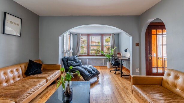 Ein modernes Wohnzimmer mit Ledersofas, einem schwarzen Ledersessel, einem Holztisch und einem großen Fenster mit Vorhängen.