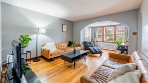 Ein modernes Wohnzimmer mit einem braunen Ledersofa, einem schwarzen Sessel, einem Couchtisch und einem Fernseher auf einem Schrank. Auf dem Couchtisch steht eine Topfpflanze und daneben am Sofa noch eine weitere.
