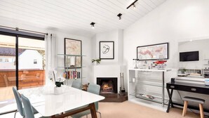 Ein modernes Wohnzimmer mit Kamin, einem Essbereich mit weißem Tisch und einem an der Wand befestigten Fernseher.