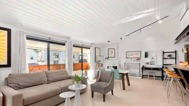 Ein modernes Wohnzimmer mit Sofa, Sessel und Couchtisch, ein Essbereich mit Tisch und Stühlen sowie eine Küchenzeile mit Arbeitsfläche und Geräten.