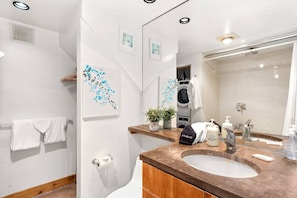 Un baño moderno con un lavamanos, un espejo y una lavadora al fondo.