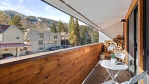 Ein Balkon mit Holzwertkasten, einem weißen Tisch und Stühlen. Vor der Wand liegt ein Holzstapel.