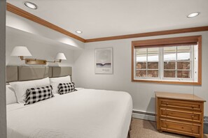 A bedroom with a large bed, a dresser, a window with a view of stone walls, and two wall-mounted lamps. - Alpenblick 09 (Aspen)
