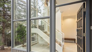 Un interior moderno con un vidrio que da a una escalera y vistas de árboles fuera.