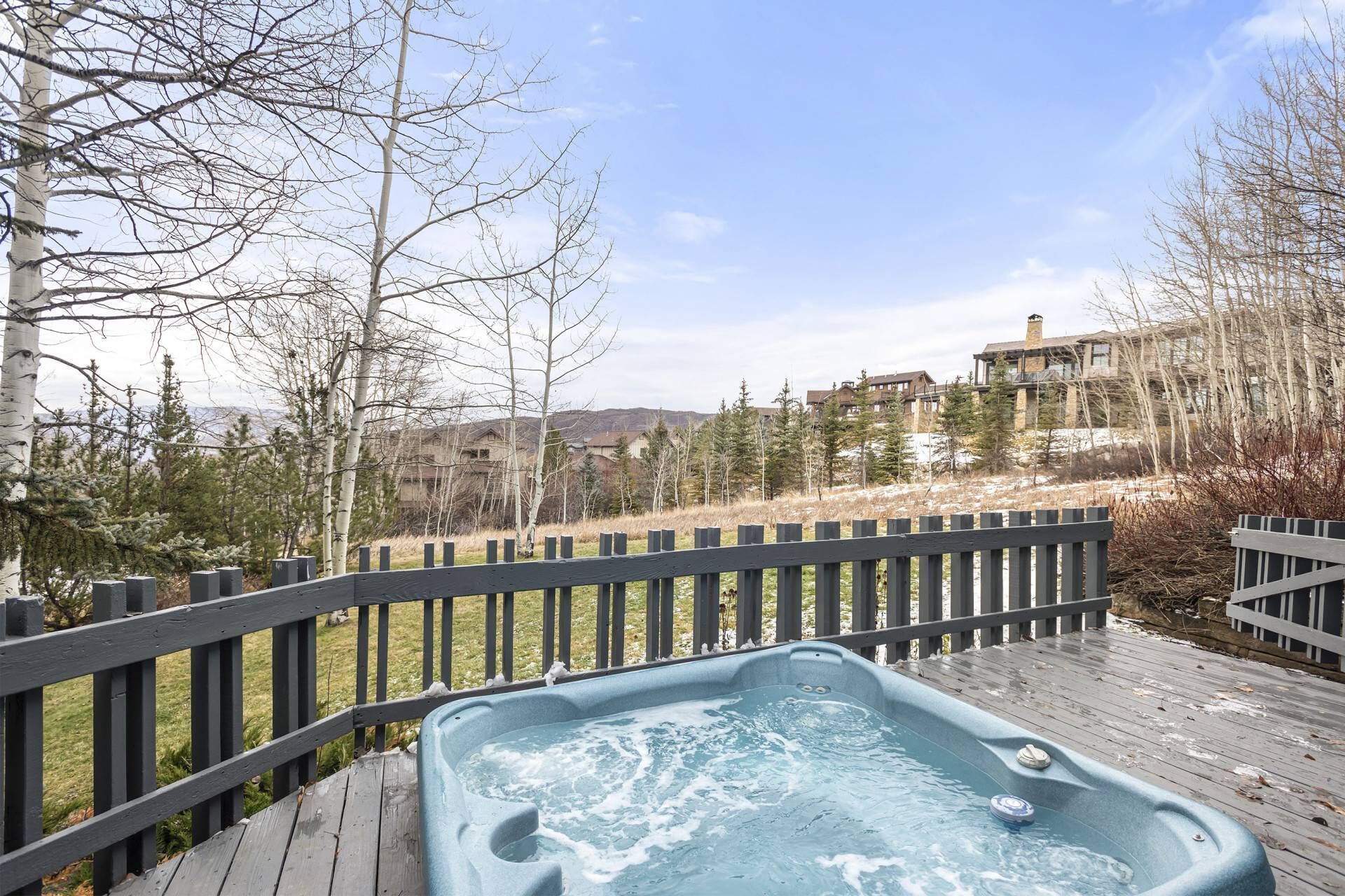 A hot tub on a wooden deck with a view of a mountainous area and buildings in the background.