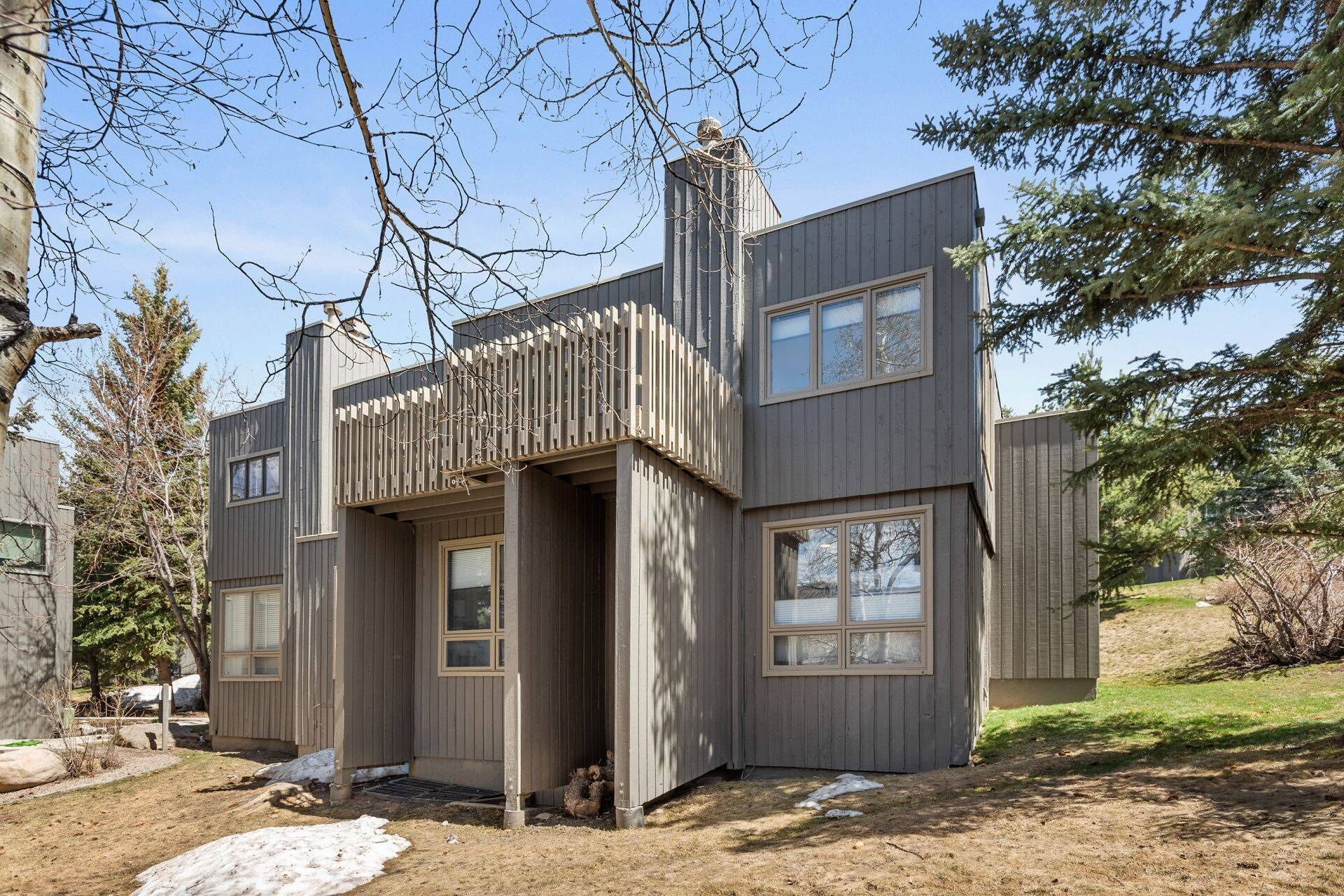 A modern, multi-level wooden house with a balcony, large windows, and a chimney.