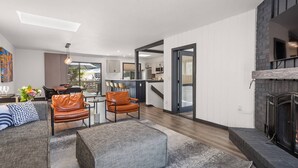 Un salon moderne avec un canapé, deux fauteuils en cuir, un pouf gris et une cheminée.