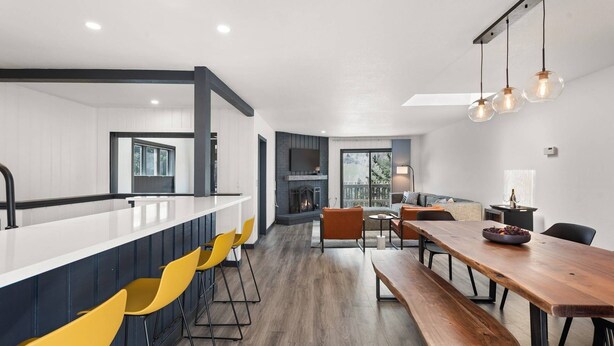Une cuisine moderne dotée d’un îlot central, de tabourets de bar et d’un coin repas avec une table et des bancs en bois.
