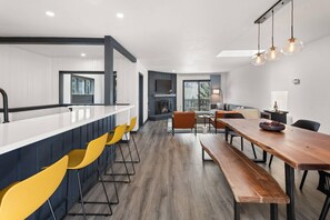 Una cocina moderna con una isla central, taburetes de bar y una zona de comedor con mesa de madera y bancos.