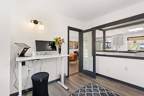 Una cocina moderna con un ventanal grande, un comedor con mesa y sillas, y una zona de trabajo con un ordenador y un jarrón de flores.
