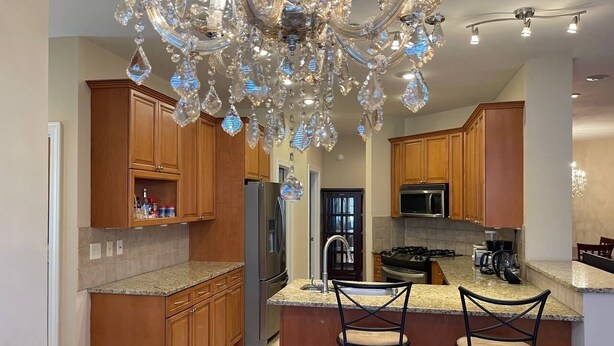 A kitchen with wooden cabinets, granite countertops, a stainless steel refrigerator, a microwave, a gas stove, and a bar area with two stools. - Luxury stay  at 4 bedroom house (Florence)