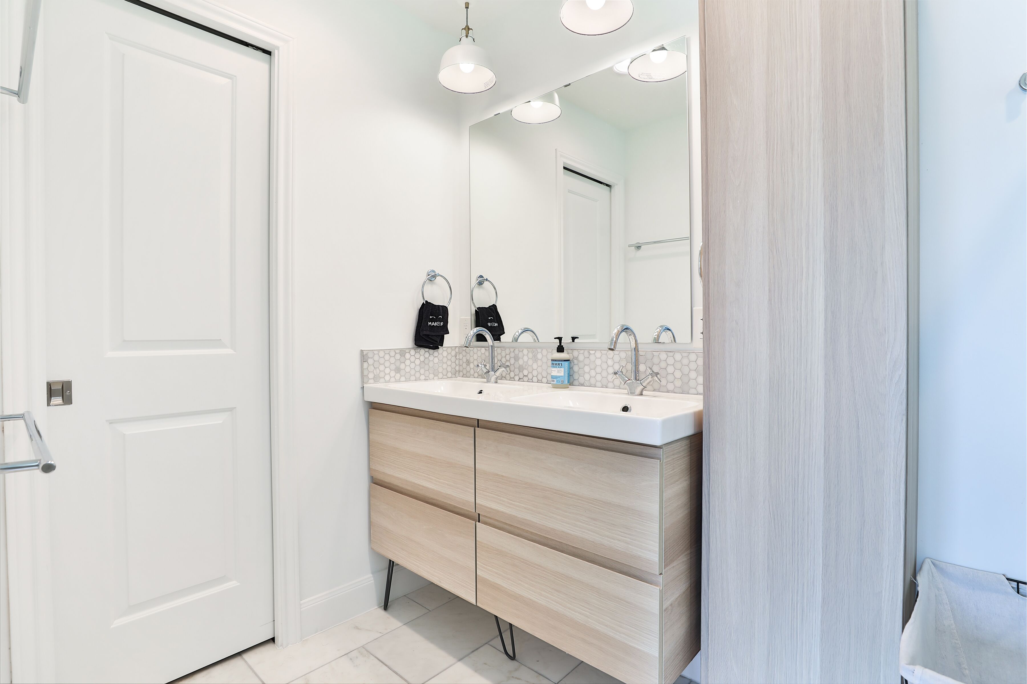 A modern bathroom with a double sink vanity, a large mirror, and a towel rack.