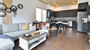 A modern living room with a grey sofa, a coffee table, and a dining area with chairs and a small table. A kitchen with dark cabinets and a microwave is visible in the background. - Modern & Comfy ~ 5 Star Location in EaDo ~ King Bed ~ Parking! Pet Friendly! (Houston)