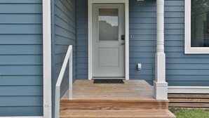 A front door with a white door and glass panel, leading to a wooden porch with a white railing. - Modern & Comfy ~ 5 Star Location in EaDo ~ King Bed ~ Parking! Pet Friendly! (Houston)
