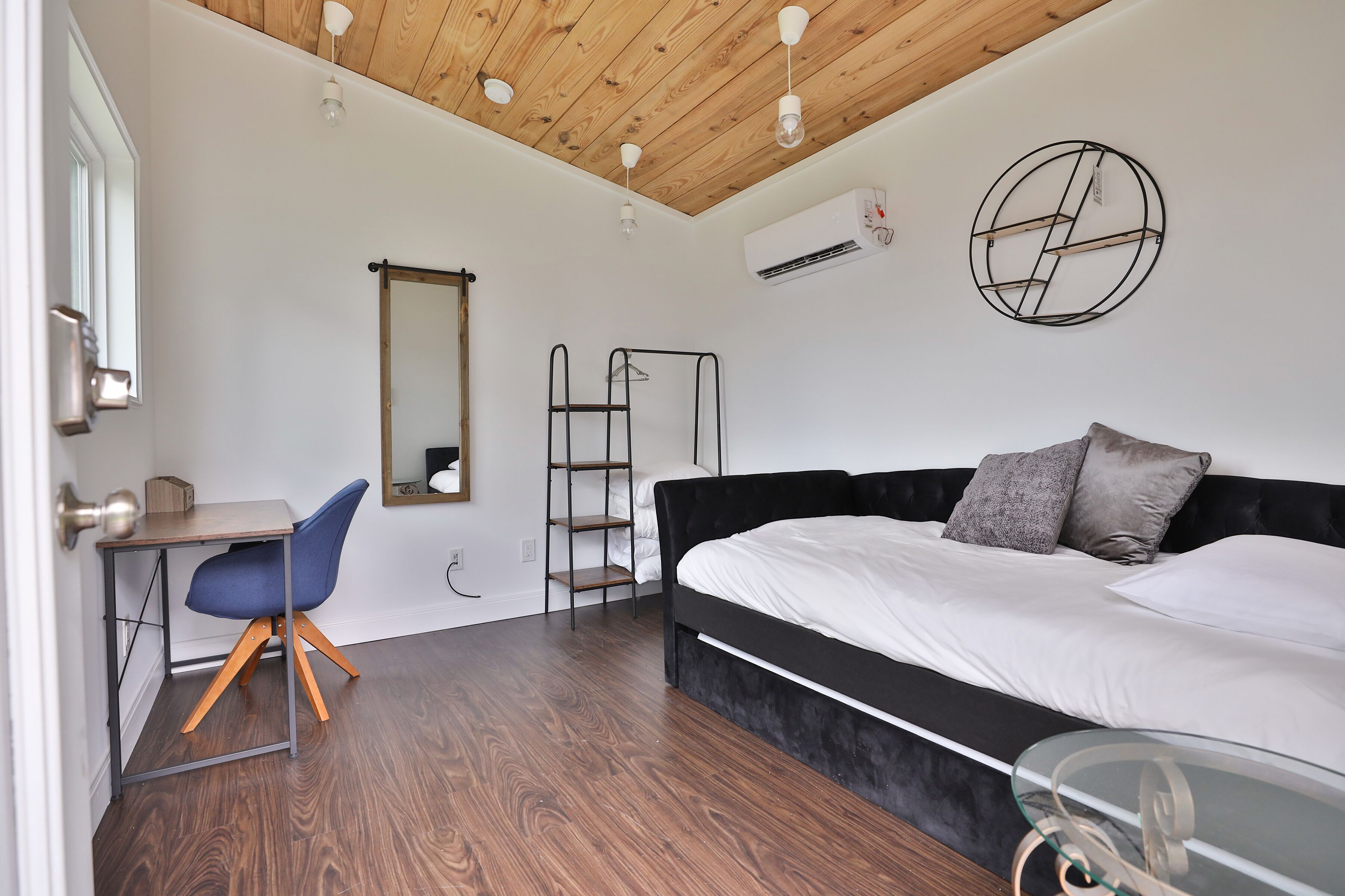 A bedroom with a bed, a desk, a chair, a ladder, and a mirror.