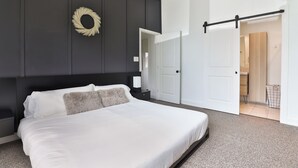 A modern bedroom with a large bed, dark walls, and a sliding door leading to a bathroom. - Modern & Comfy ~ 5 Star Location in EaDo ~ King Bed ~ Parking! Pet Friendly! (Houston)
